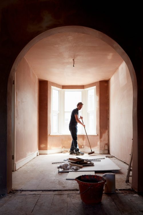 A builder sweeping and tidying up in a renovated replastered house with an archway.