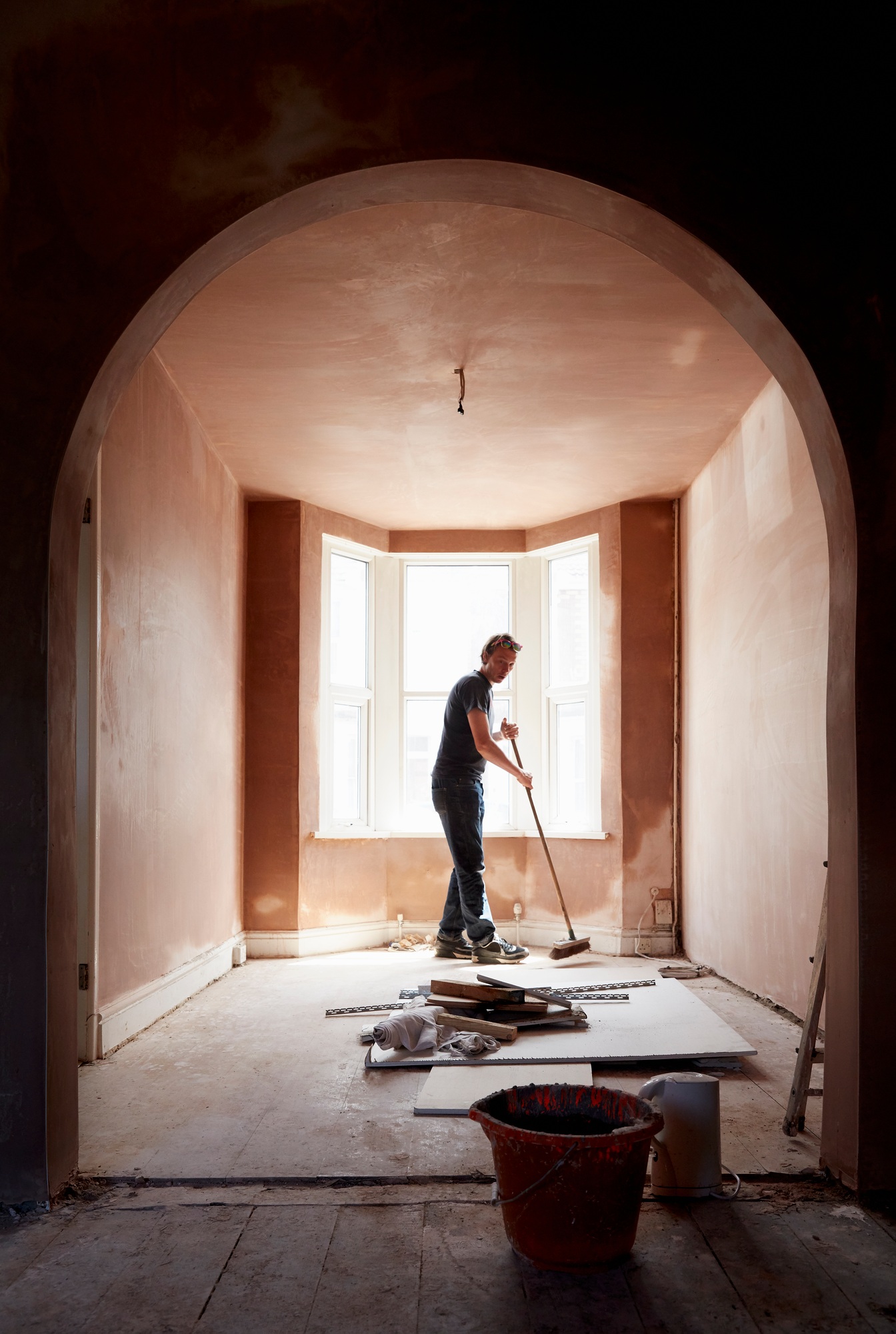 A builder sweeping and tidying up in a renovated replastered house with an archway.